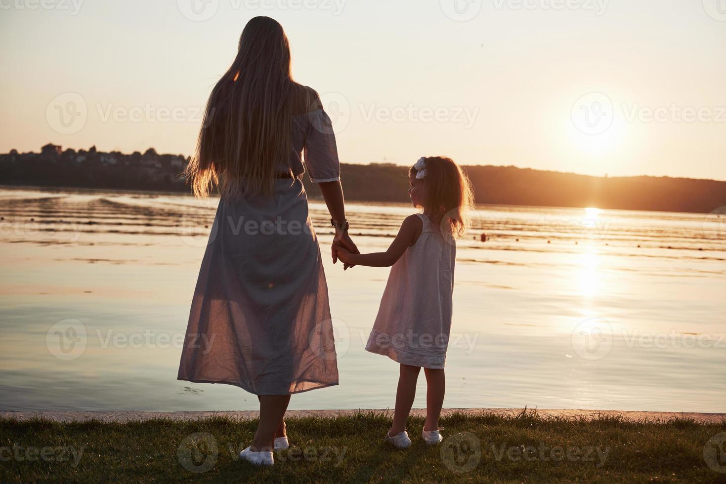 la mamma gioca con il suo bambino in vacanza vicino all'oceano, sagome al tramonto foto