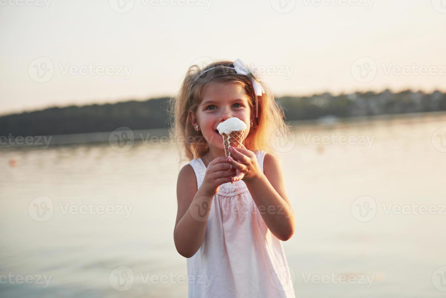 una bellissima bambina mangia un gelato vicino all'acqua foto