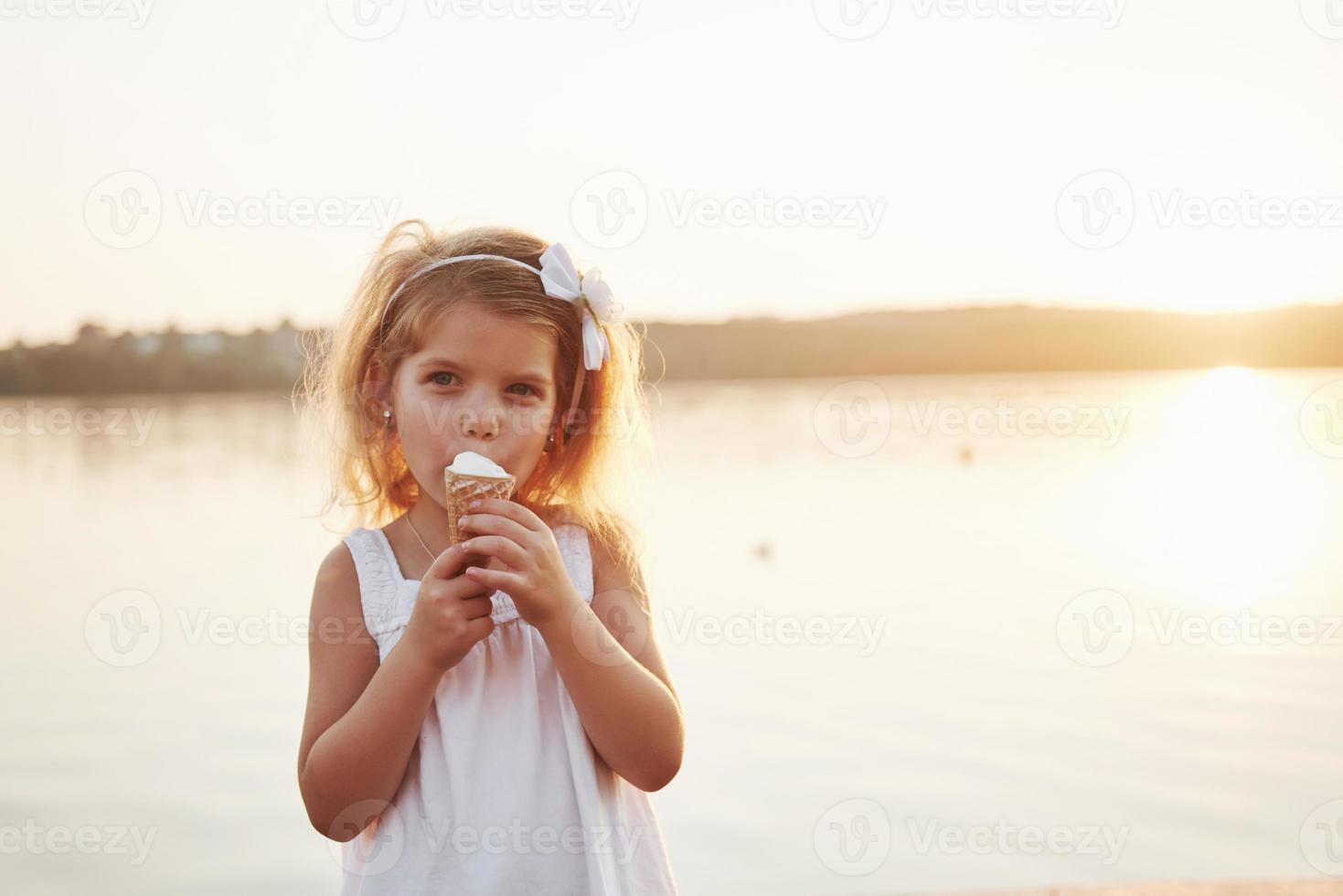 una bellissima bambina mangia un gelato vicino all'acqua foto