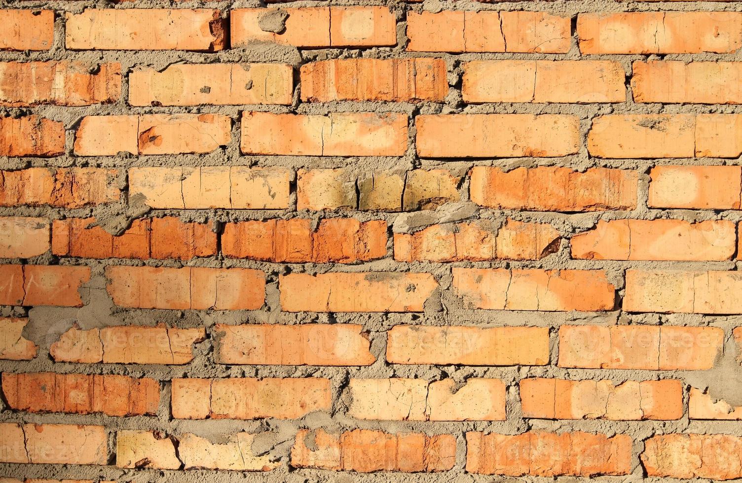 nuovo muro di mattoni, color terracotta con resti di cemento e cuciture grossolane, illuminato da un sole splendente. foto