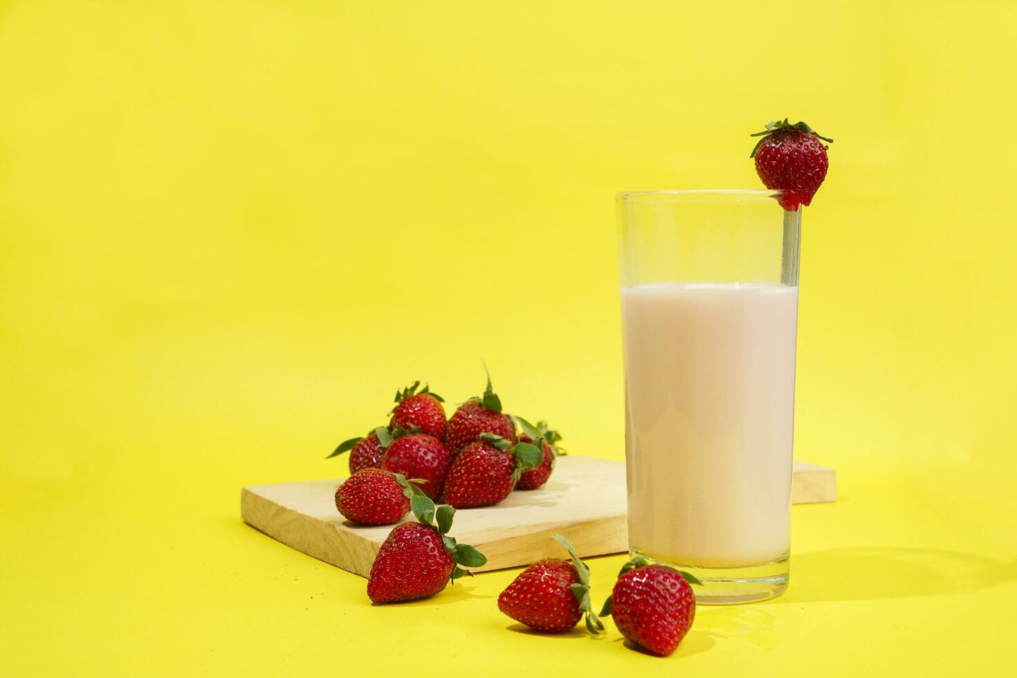 un' bicchiere di latte con fragola contorno su tagliare tavola isolato giallo sfondo foto