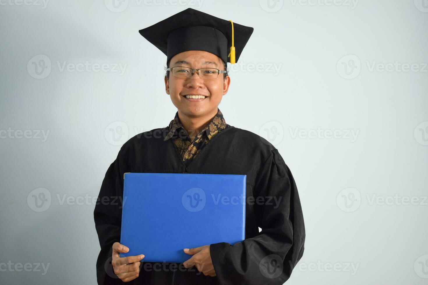 espressive di adulto Indonesia maschio indossare la laurea veste, cappello e occhiali, asiatico maschio la laurea portare vuoto blu certificato isolato su bianca sfondo, espressioni di ritratto la laurea foto