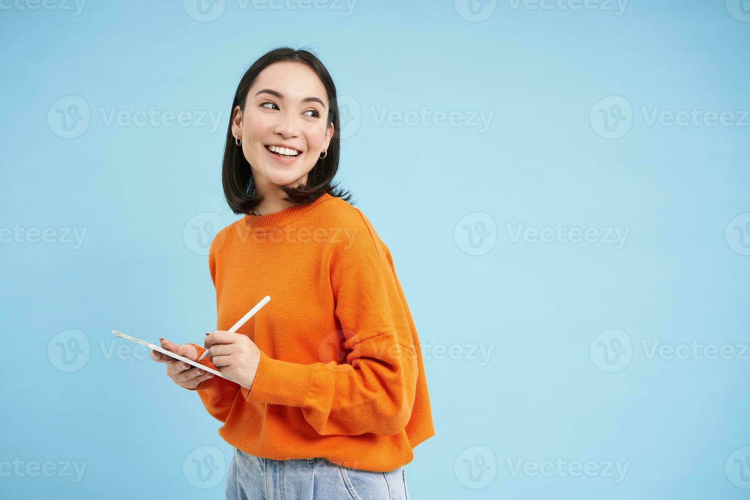 ritratto di giovane Cinese donna, insegnante o alunno con digitale tavoletta e matita, scrivere, assunzione Appunti, fare sua compiti a casa, in piedi al di sopra di blu sfondo foto