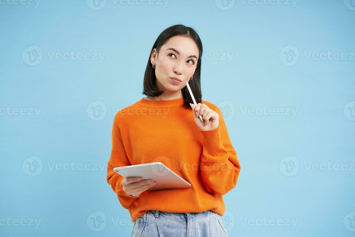ritratto di giovane Cinese donna, insegnante o alunno con digitale tavoletta e matita, scrivere, assunzione Appunti, fare sua compiti a casa, in piedi al di sopra di blu sfondo foto