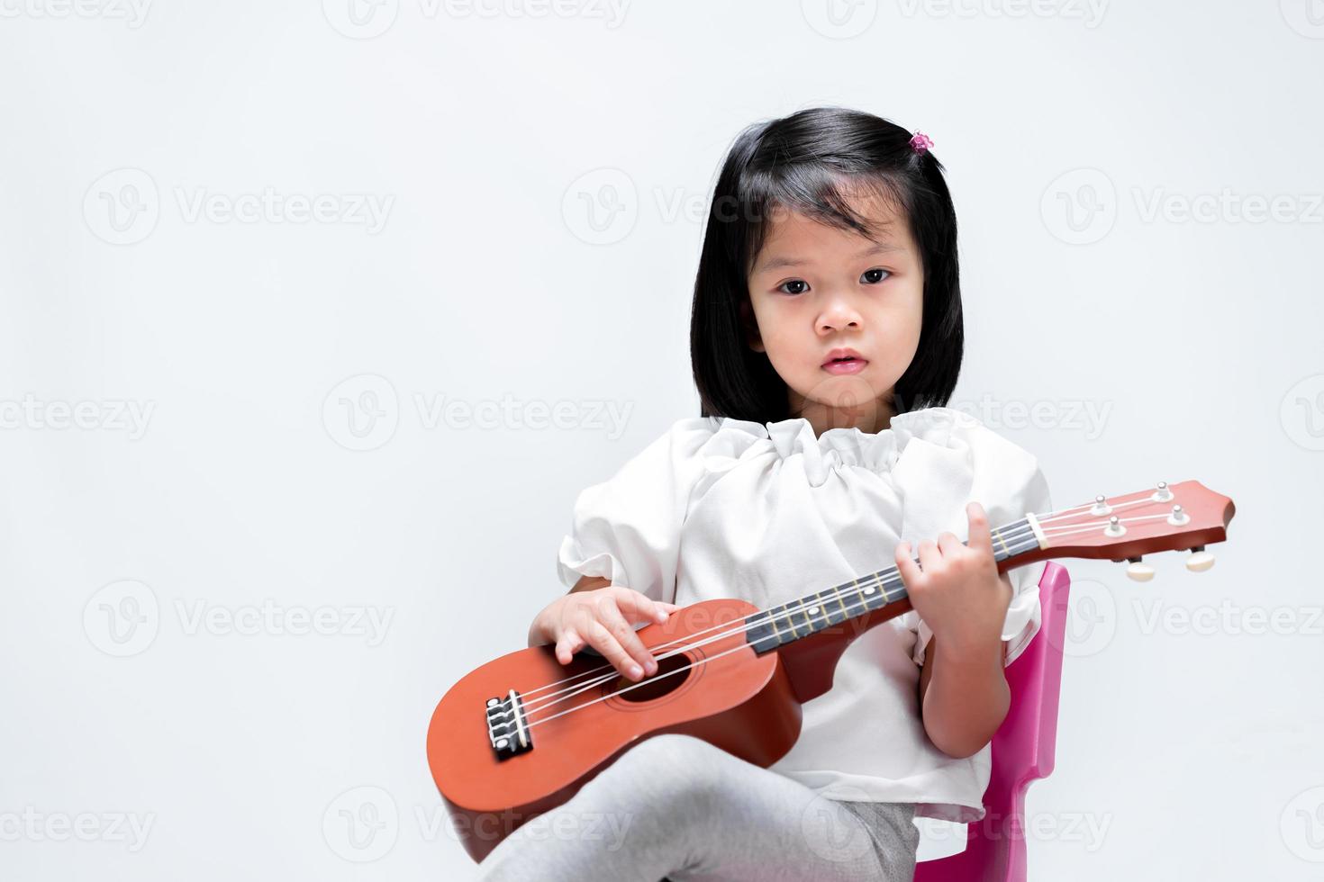 bambina carina che gioca ukulele marrone in studio su sfondo bianco. foto