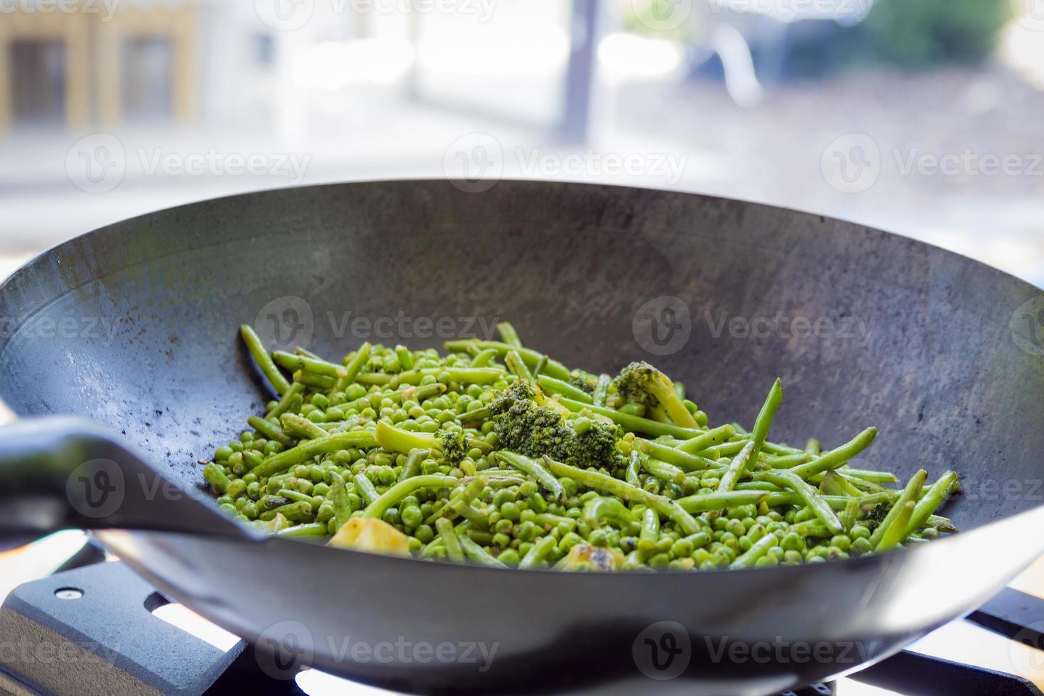 close up su fagiolini, broccoli e piselli vengono cotti in una grande padella di ferro foto