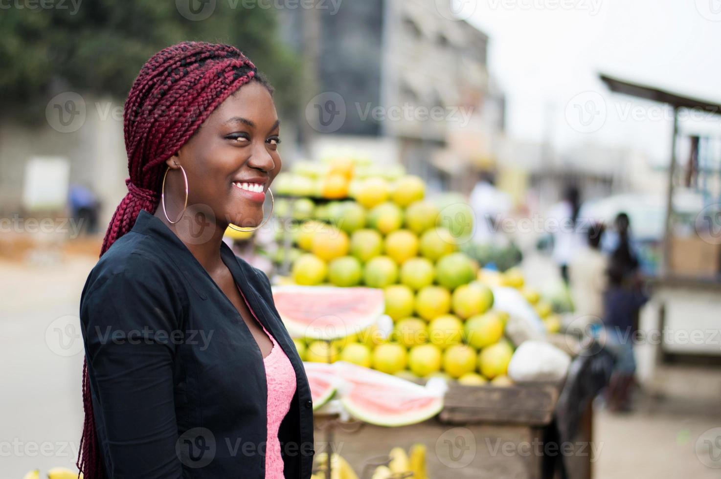 ritratto di giovane donna sorridente in piedi vicino a scaffali di frutta. foto