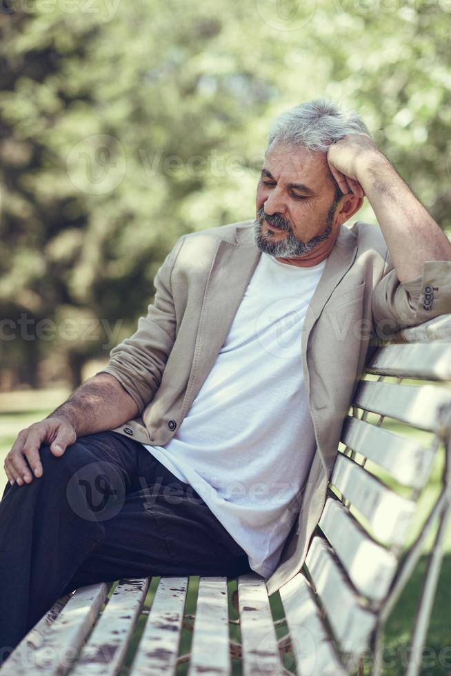 pensieroso uomo maturo seduto su una panchina in un parco urbano. foto