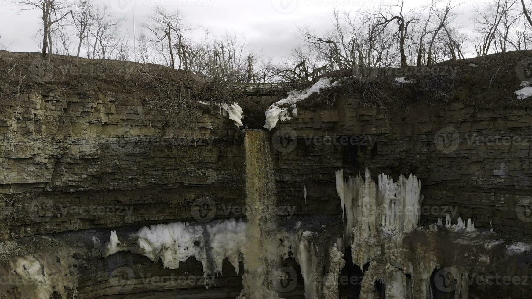 aereo per piccolo giallo acqua ruscello immergendosi giù a il scogliere con sporco ghiaccio su scogliera piste. scorta. ripido pendenza di alto cava con sporco acqua caduta fuori uso, naturale sfondo. foto