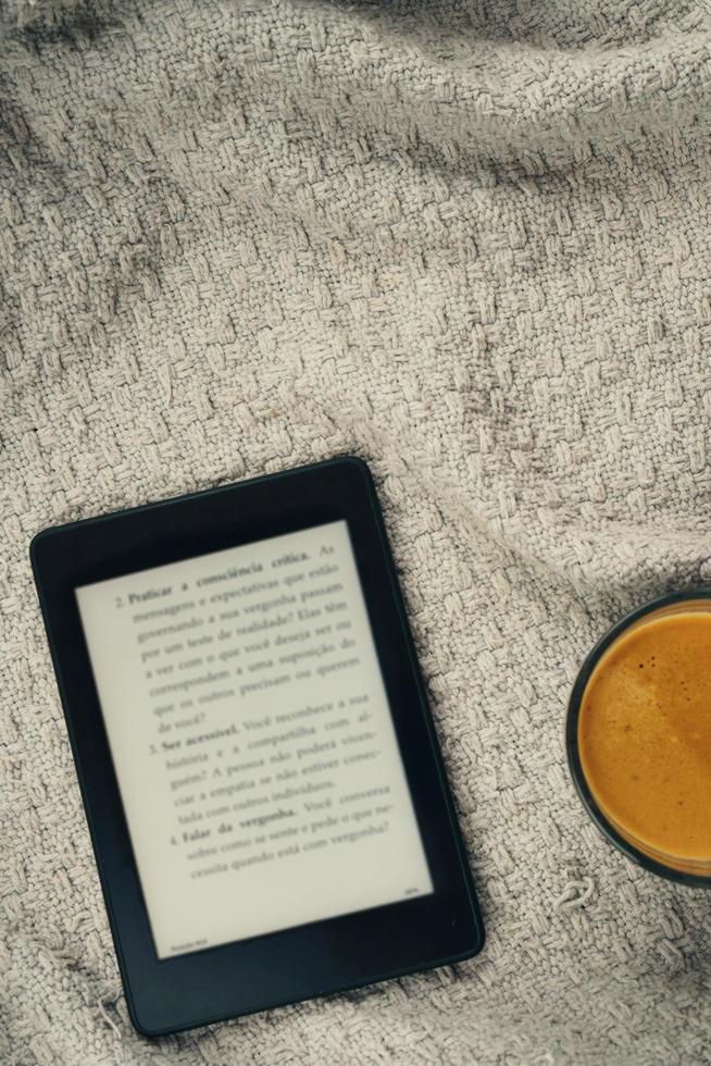 lettore di e-book, una tazza di caffè e un auricolare foto