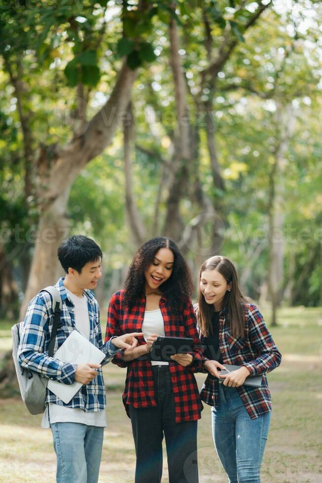 tre giovane Università studenti è lettura un' libro mentre rilassante seduta su erba nel un' città universitaria parco con sua gli amici. formazione scolastica concetto foto