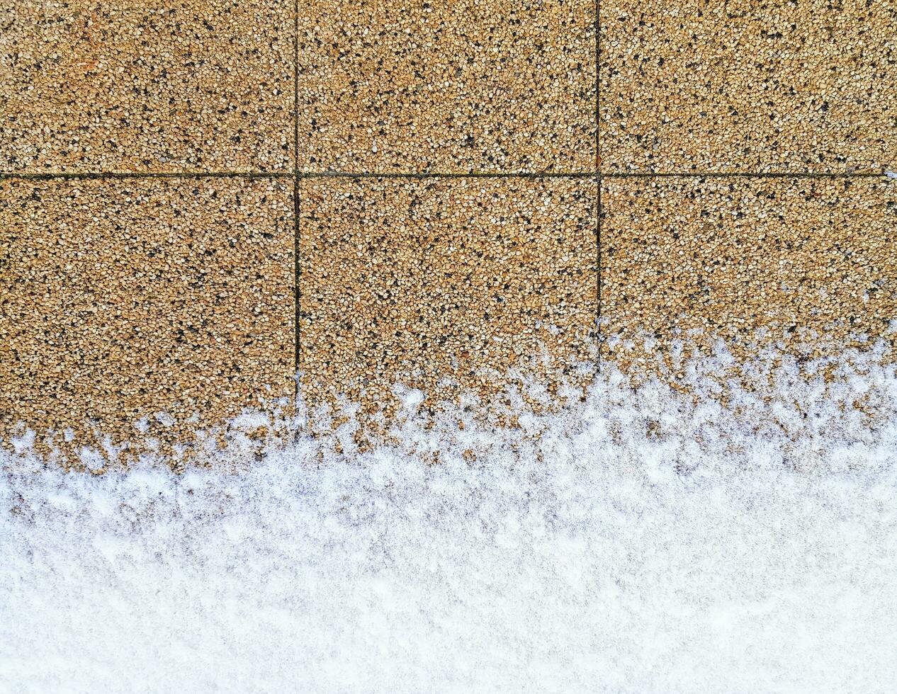 marciapiede parzialmente coperto con neve a il parte inferiore. pavimentazione lastre fatto di molto piccolo ciottoli, Marrone e beige. marciapiede orizzontale sfondo. posto per il tuo testo Qui foto