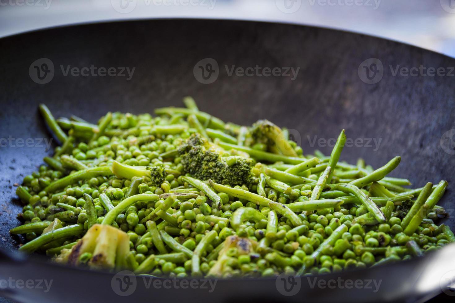 close up su fagiolini, broccoli e piselli vengono cotti in una grande padella di ferro foto