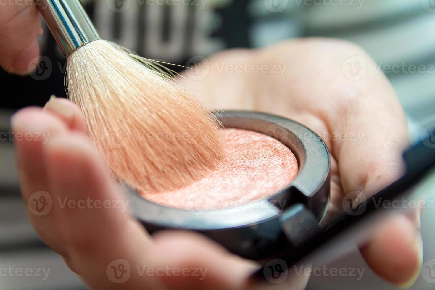 primo piano delle mani della donna che tengono il pennello per il trucco e la scatola del fard foto