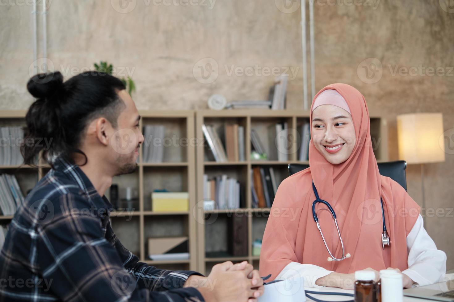 giovane bella donna medico sta esaminando la salute del paziente maschio in ufficio della clinica ospedaliera e consigliando con un sorriso sui farmaci. questo medico specialista asiatico è una persona islamica che indossa un hijab. foto