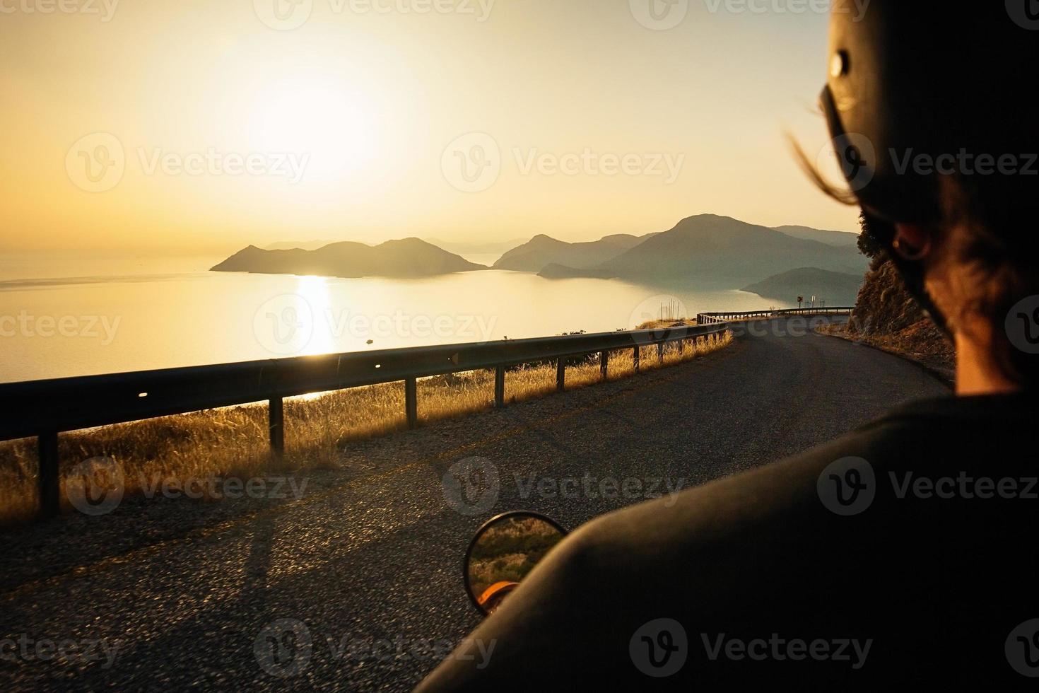 motociclista che guida lungo la strada di montagna al tramonto sul mare, movimento sfocato foto