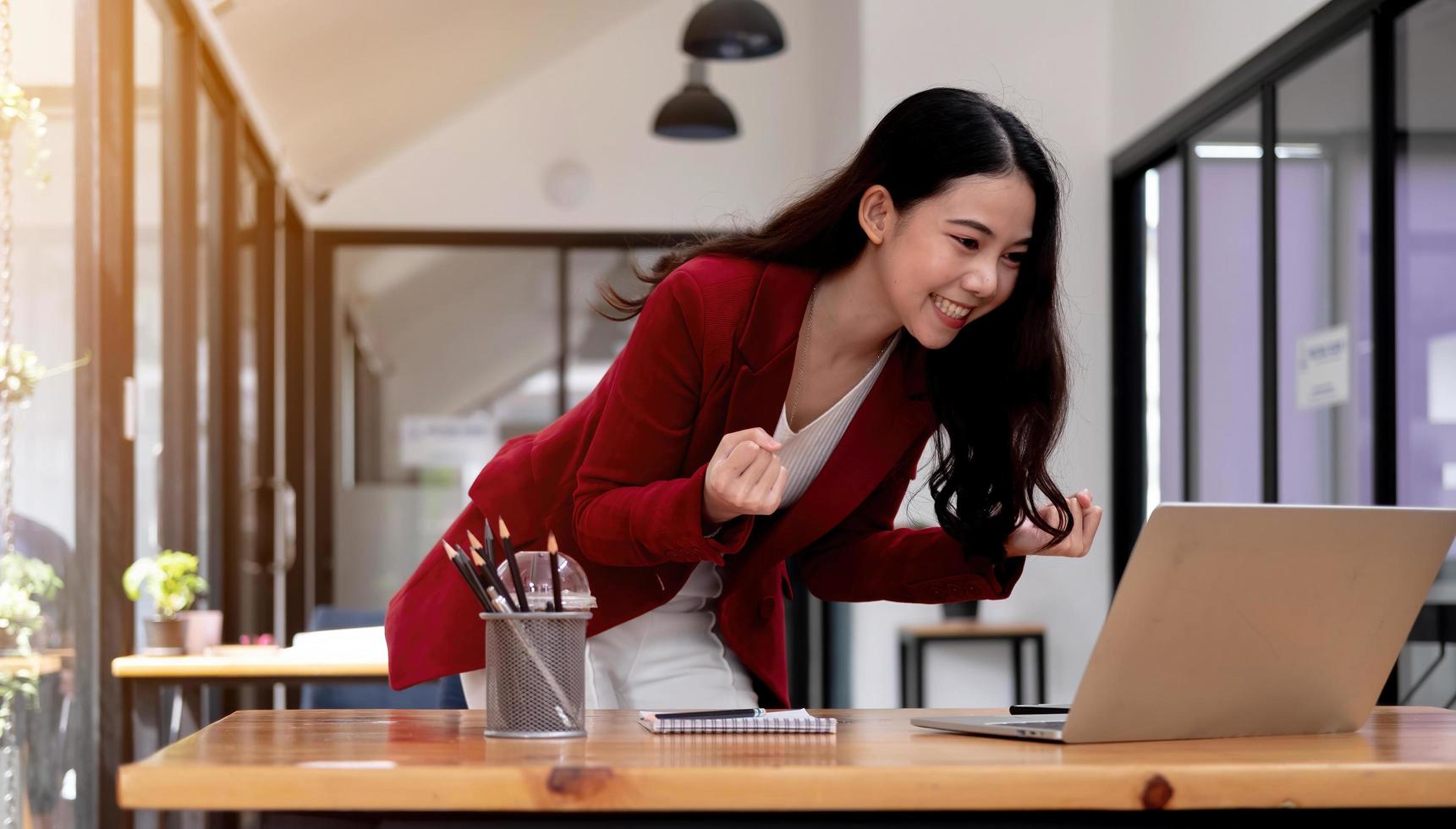 ritratto di donna asiatica di affari di successo godere di successo con il computer portatile sulla scrivania. colpo autentico donna gioiosa ha ottenuto il jackpot, sorpreso e celebrando la sua vittoria. foto