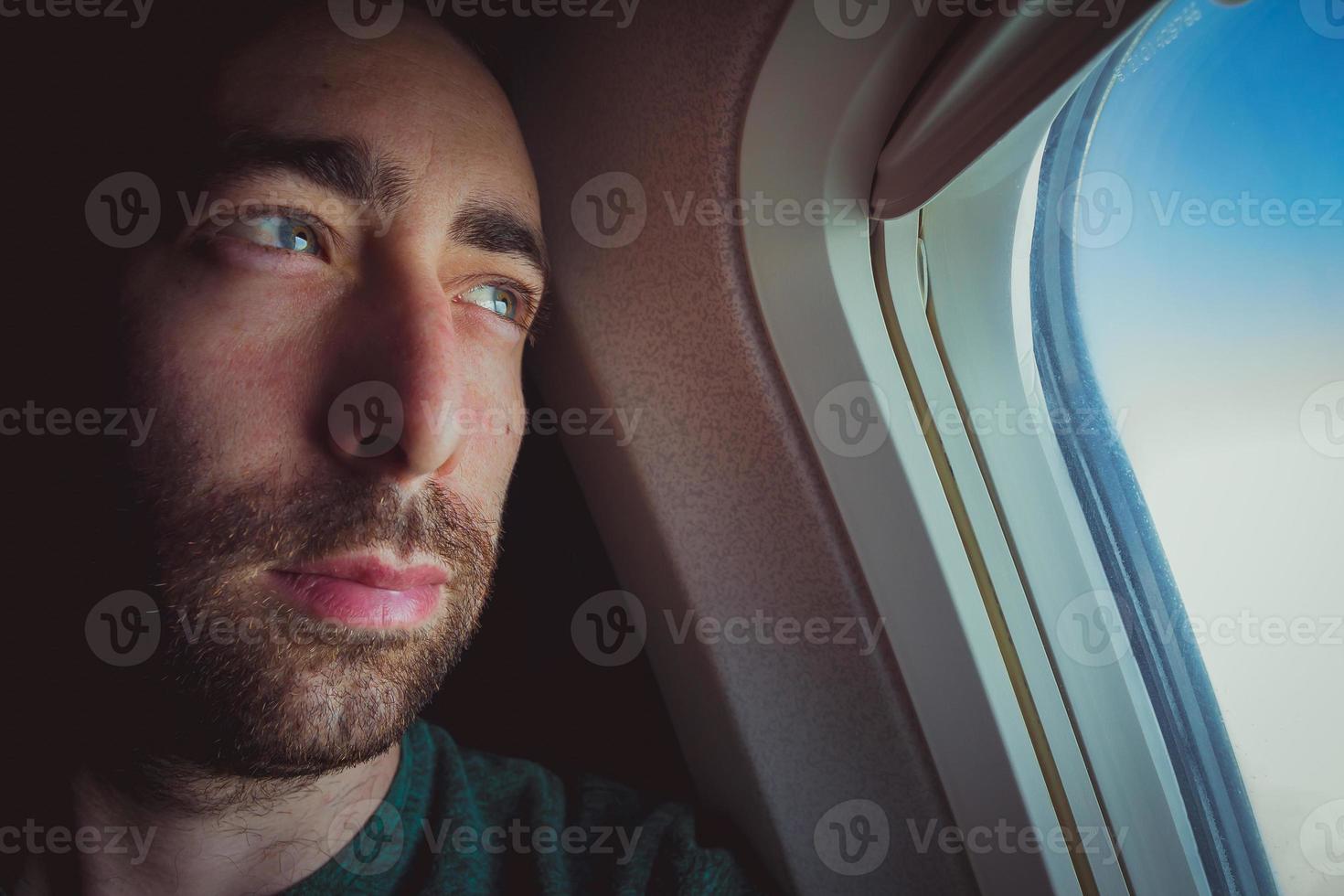 primo piano di un uomo pensieroso che guarda fuori attraverso il finestrino di un aeroplano foto