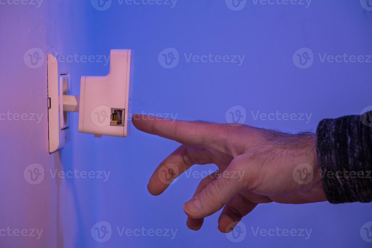 l'uomo preme con il dito sul pulsante wps sul ripetitore wifi che si trova nella presa elettrica a muro foto