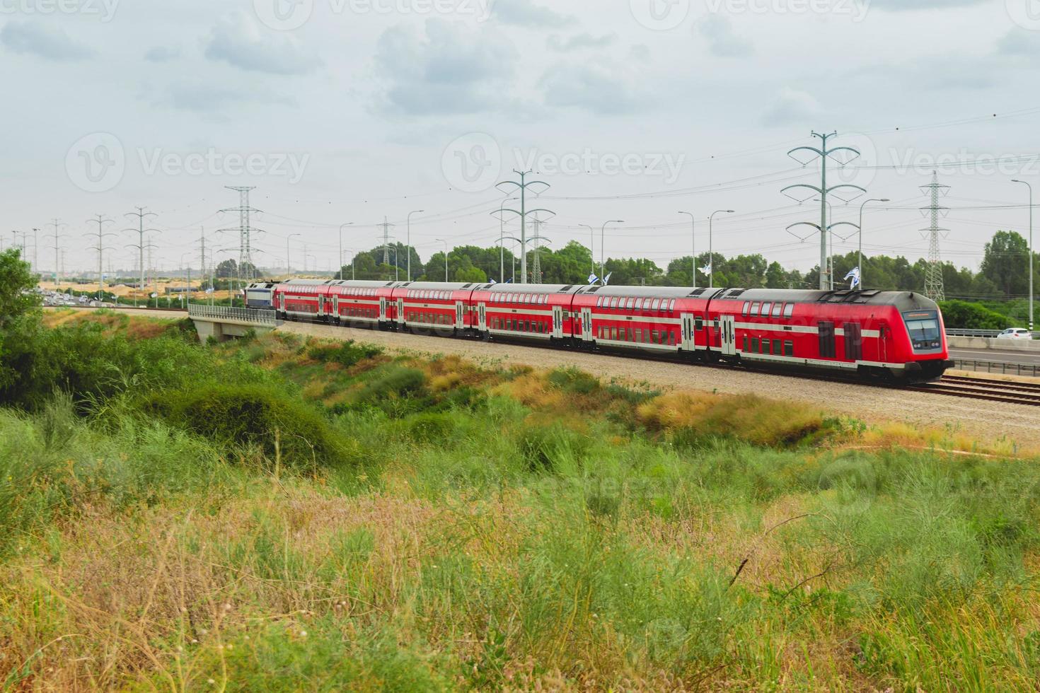 treno passeggeri israeliano rosso in movimento fuori città vicino all'autostrada 4 foto