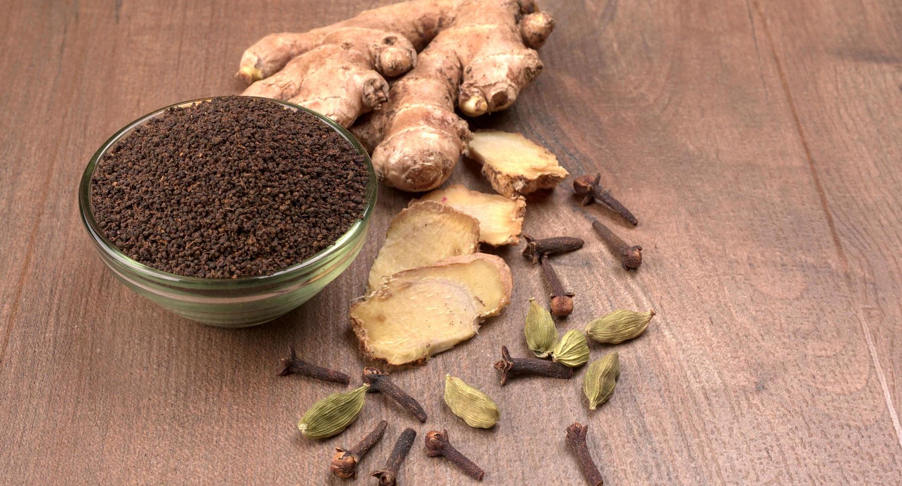 tè nero in polvere o polvere secca di tè in polvere, chai patti isolati in una ciotola di legno con cardamomo, chiodi di garofano e zenzero. foto