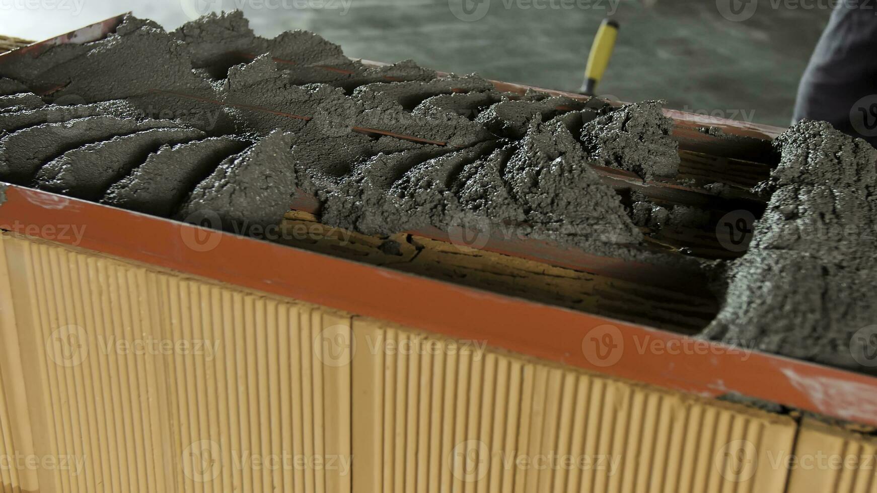 costruzione lavoratore posa crudo cemento con un' cazzuola e speciale telaio. azione filmato. vicino su di crudo mortaio essere mettere su ceramica blocchi. foto