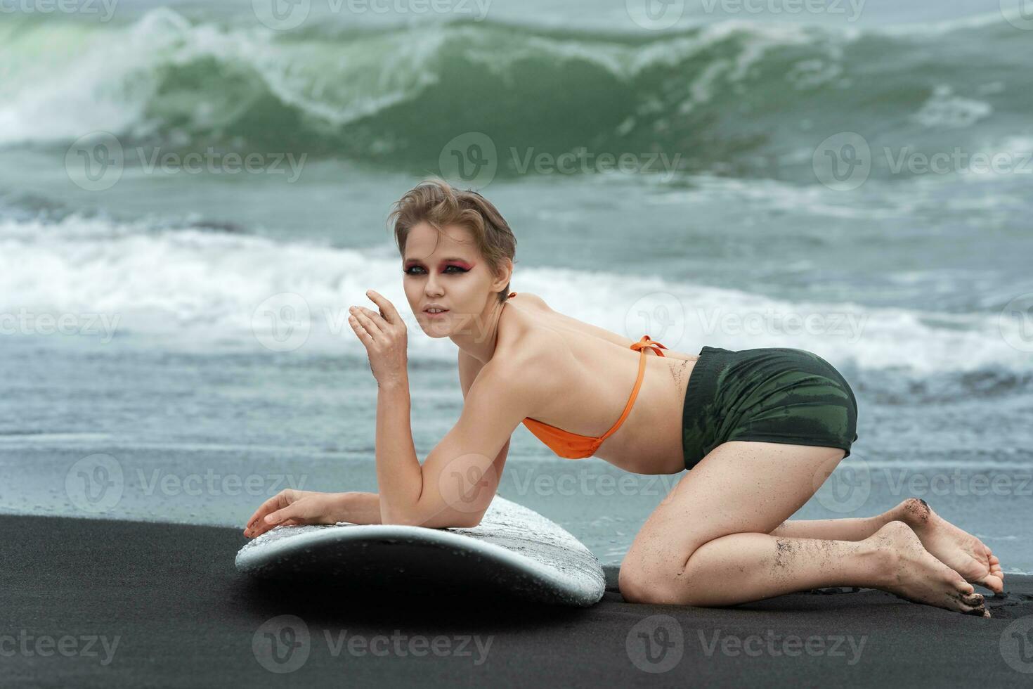 sensualità flessibilità di donna surfista. lei scioperi fiducioso posa con fidato tavola da surf su spiaggia foto