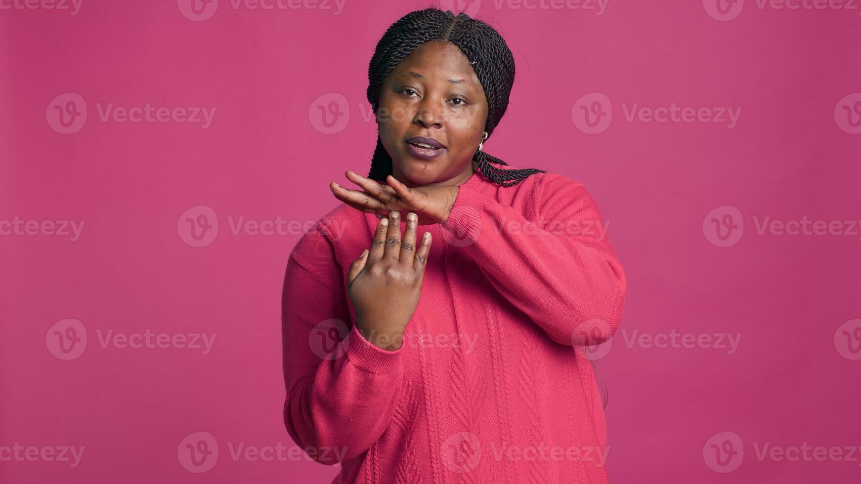 espressive giovane nero donna mostrando tempo scaduto cartello utilizzando sua mani nel davanti di rosa sfondo. africano americano bellezza visualizzazione pausa-pausa segnale con corpo linguaggio in direzione telecamera. foto