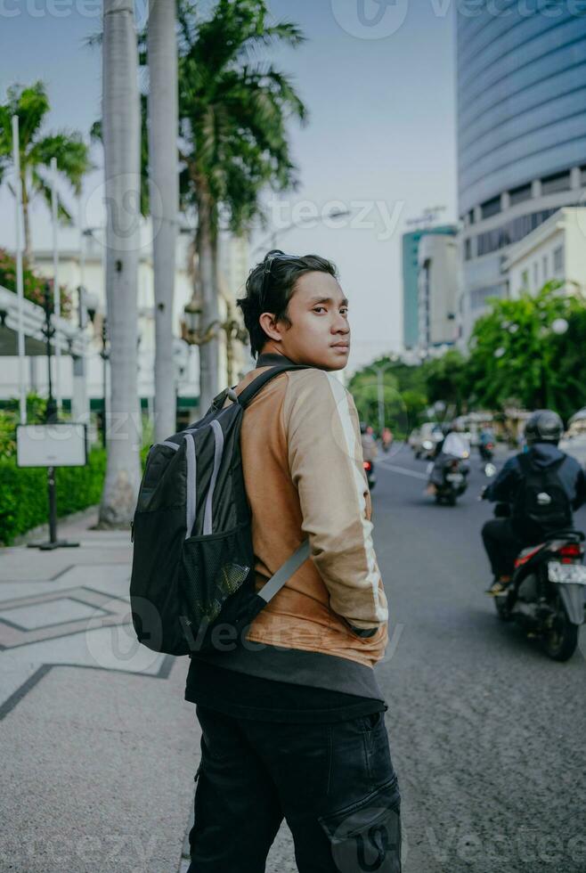 asiatico maschio turista in viaggio solo assunzione zaino nel urbano la zona. palma alberi e urbano. viaggio e vacanza concetto sfondo. foto