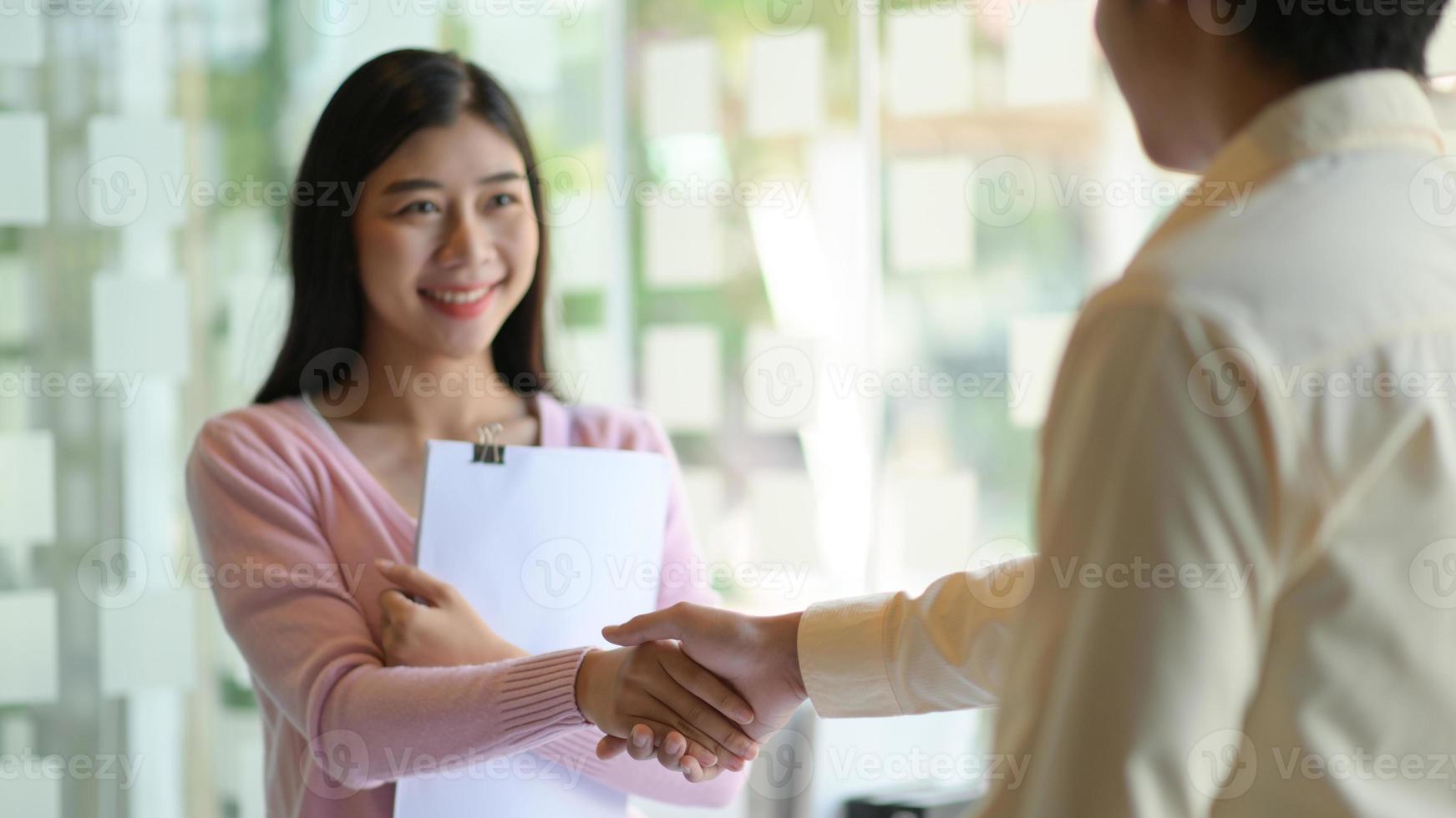 giovani donne e uomini si stringono la mano per congratularsi e sorridere felicemente nell'ufficio moderno. foto