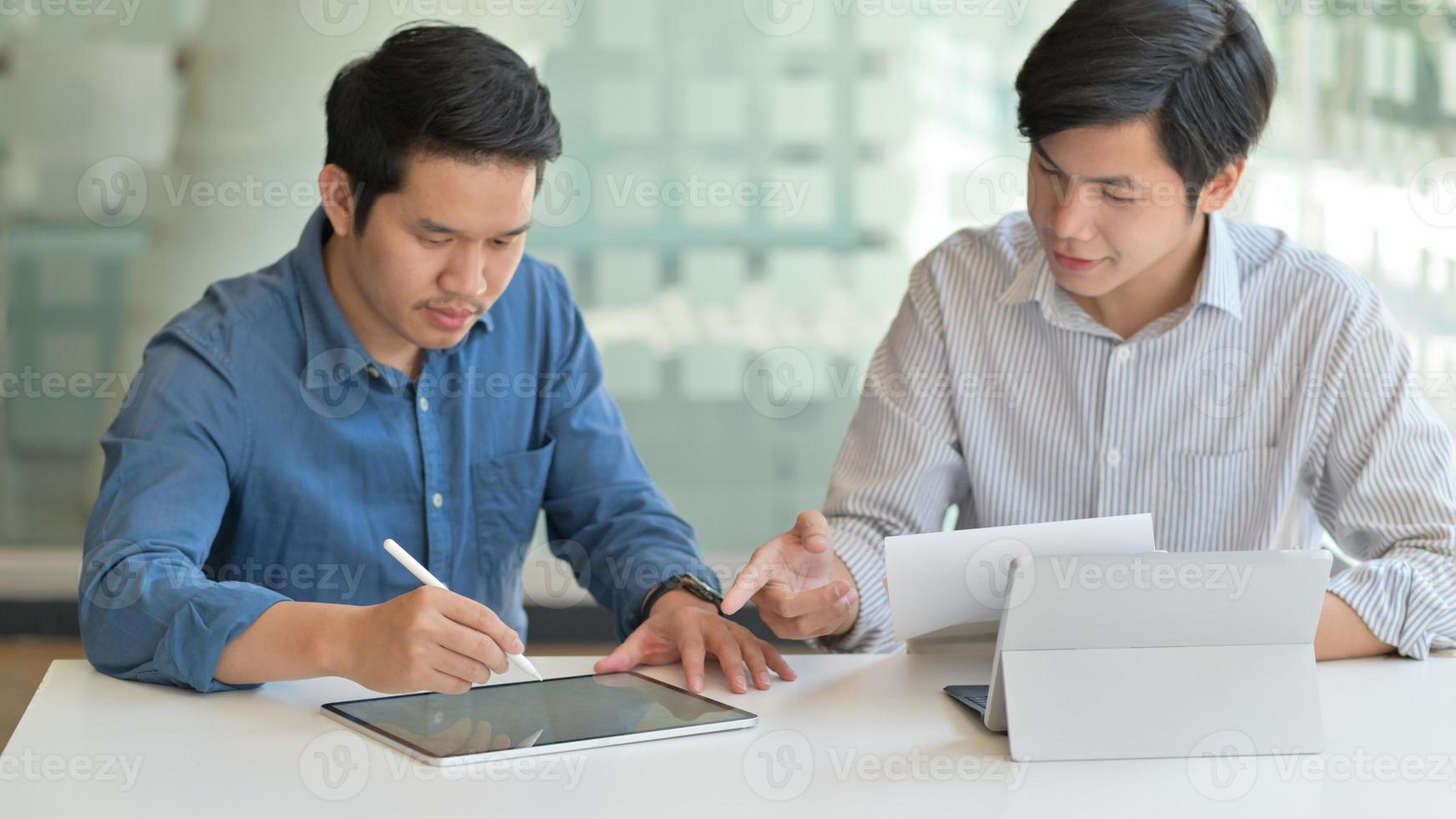 due uomini asiatici usano il tablet per creare il loro lavoro per presentare i clienti in un ufficio contemporaneo. foto
