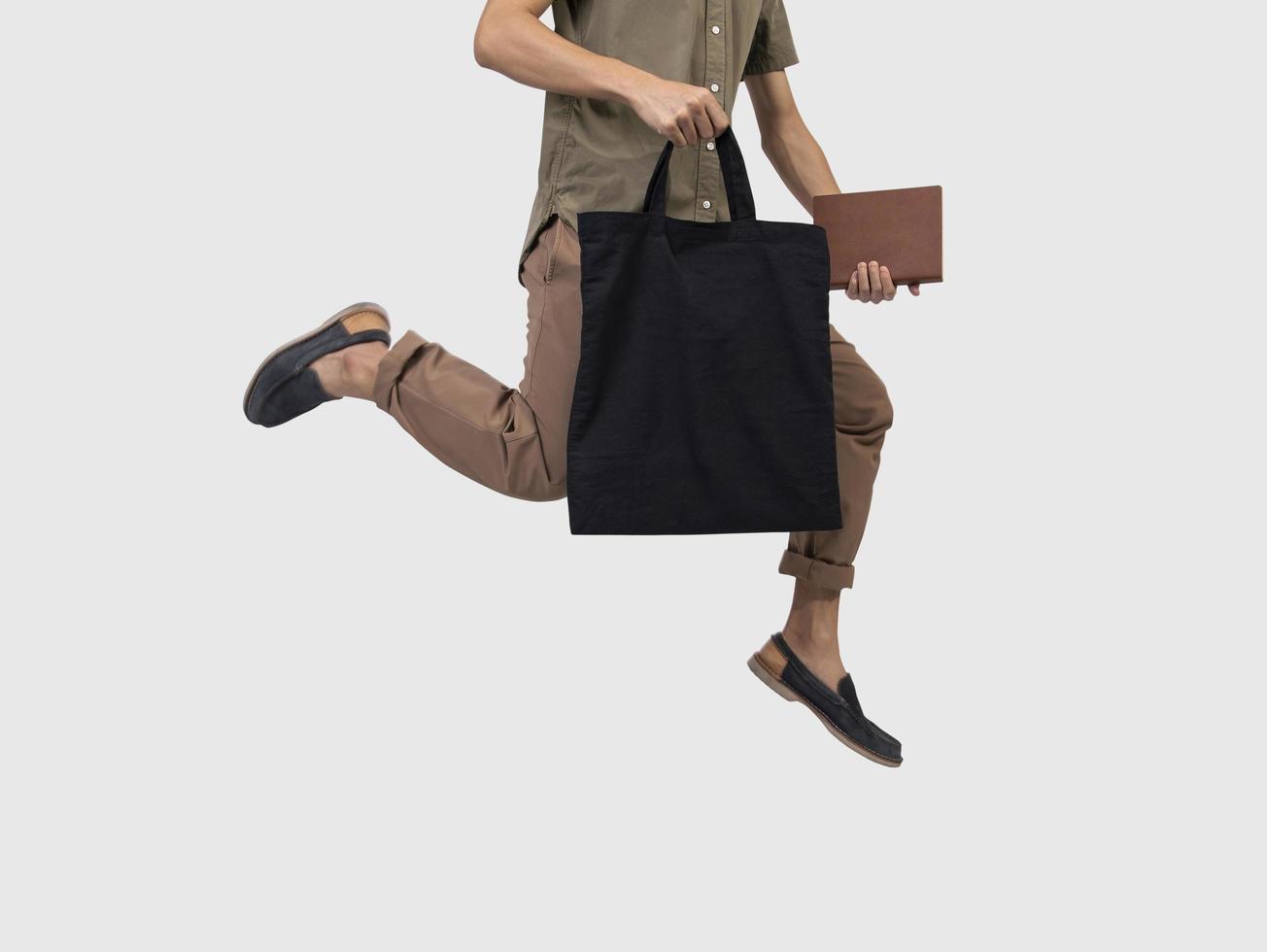 il salto dell'uomo sta tenendo il tessuto della tela della borsa per il modello in bianco del modello isolato su fondo grigio. foto