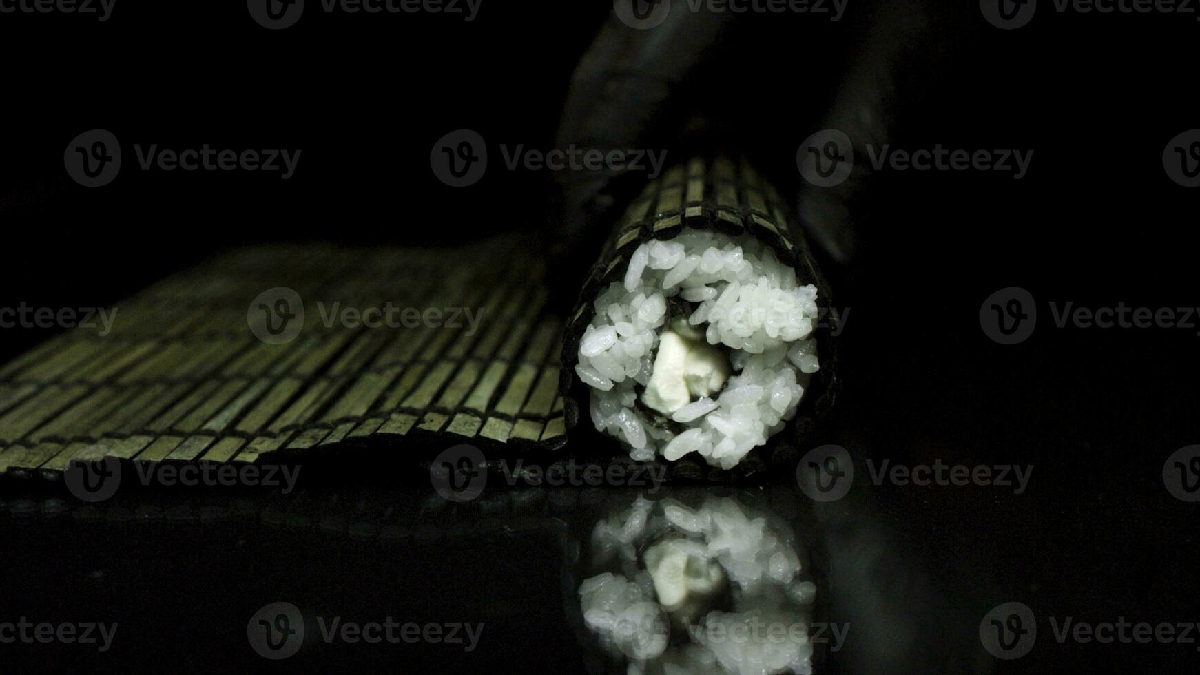 Sushi rotolamento processi con nero bambù makisu, isolato su nero sfondo. mani nel nero guanti rotolamento Sushi con nero bambù stuoia, cucinando concetto. foto