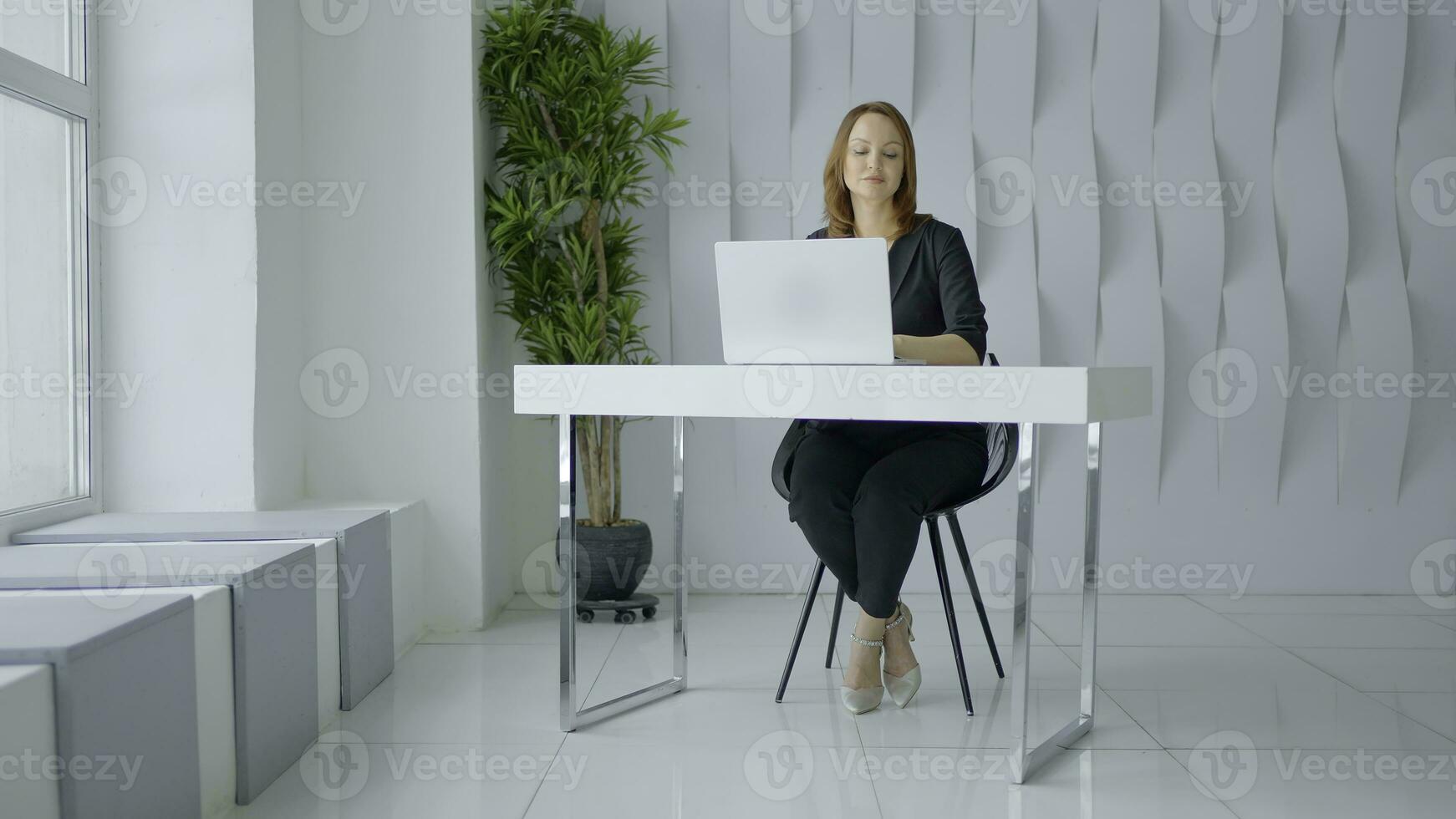 donna nel completo da uomo Lavorando nel un' moderno ufficio a il tavolo. azione. bianca muri, verde pianta e un' tavolo con un' computer portatile, minimalista stile. foto