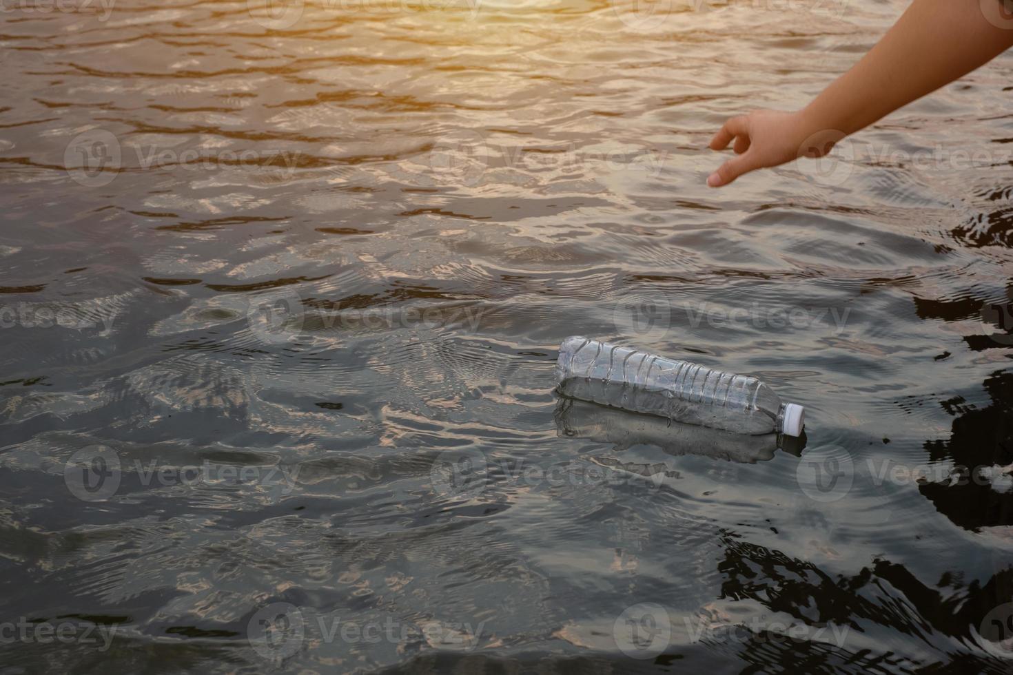 mano della donna per raccogliere la bottiglia di plastica dei rifiuti usata sull'acqua in un canale foto