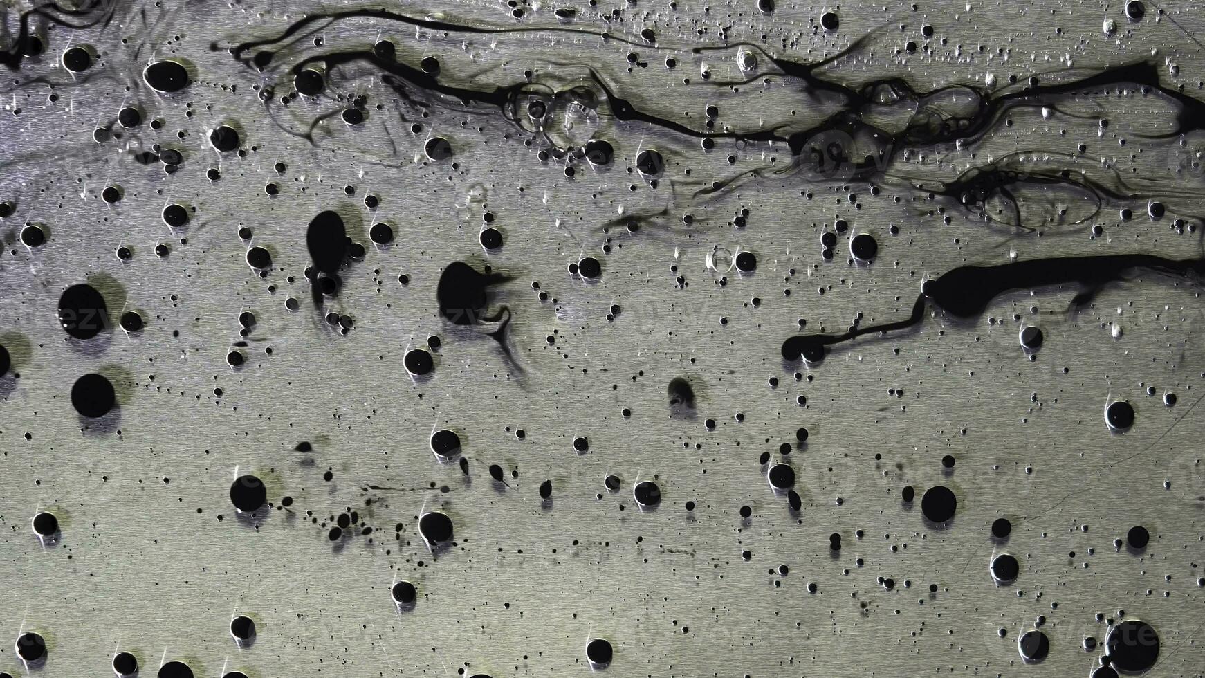 superiore Visualizza di nero inchiostro gocce fluente nel liquido olio su metallico, grigio sfondo. nero palle di dipingere galleggiante su il oleoso sostanza superficie. foto