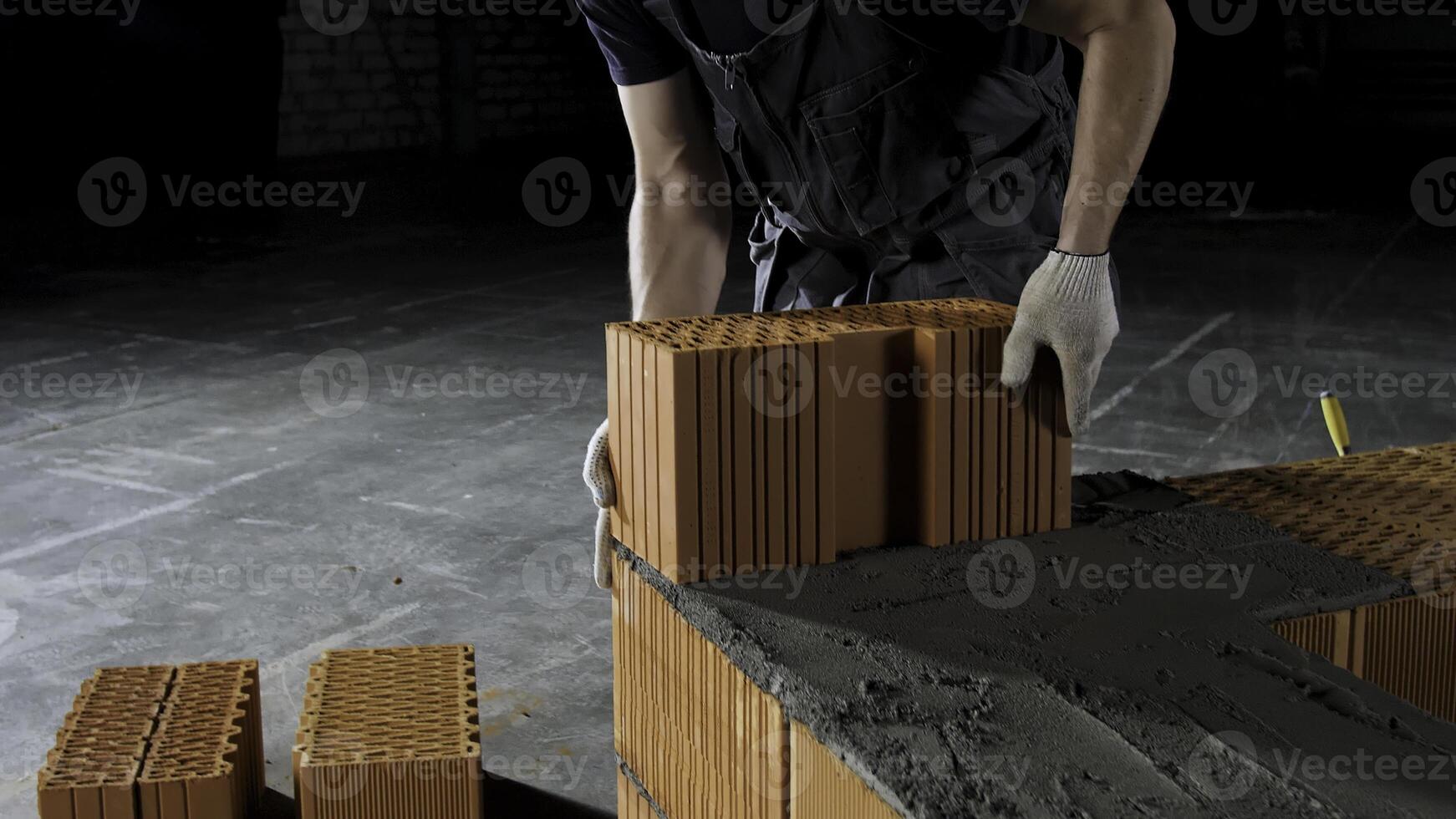 muratore Lavorando a il costruzione luogo, fabbricazione un altro strato di un' mattone parete. azione filmato. muratore mettendo giù rosso mattone su cemento seminterrato. foto