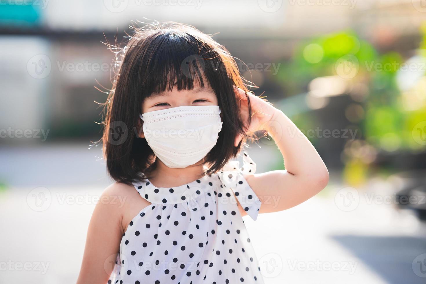 una giovane ragazza che indossa una maschera bianca è in piedi a grattarsi la testa mentre suda per il caldo sole della sera. foto