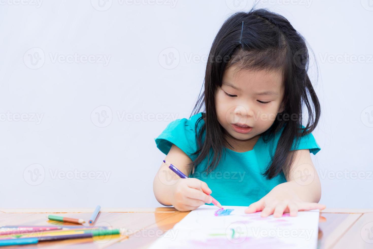 la ragazza sta facendo arte sul libro da colorare con i colori del legno. il bambino si diverte a fare mestieri. praticare la creatività nei bambini. studiare a casa. I bambini di 3-4 anni indossano abiti verdi. sfondo muro bianco isolato. foto