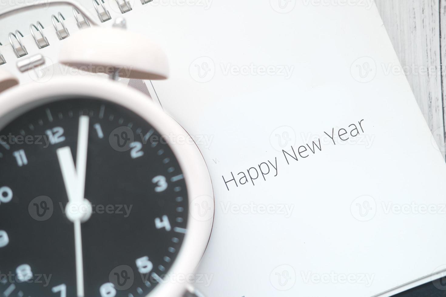 testo di felice anno nuovo sul calendario con l'orologio sul tavolo foto