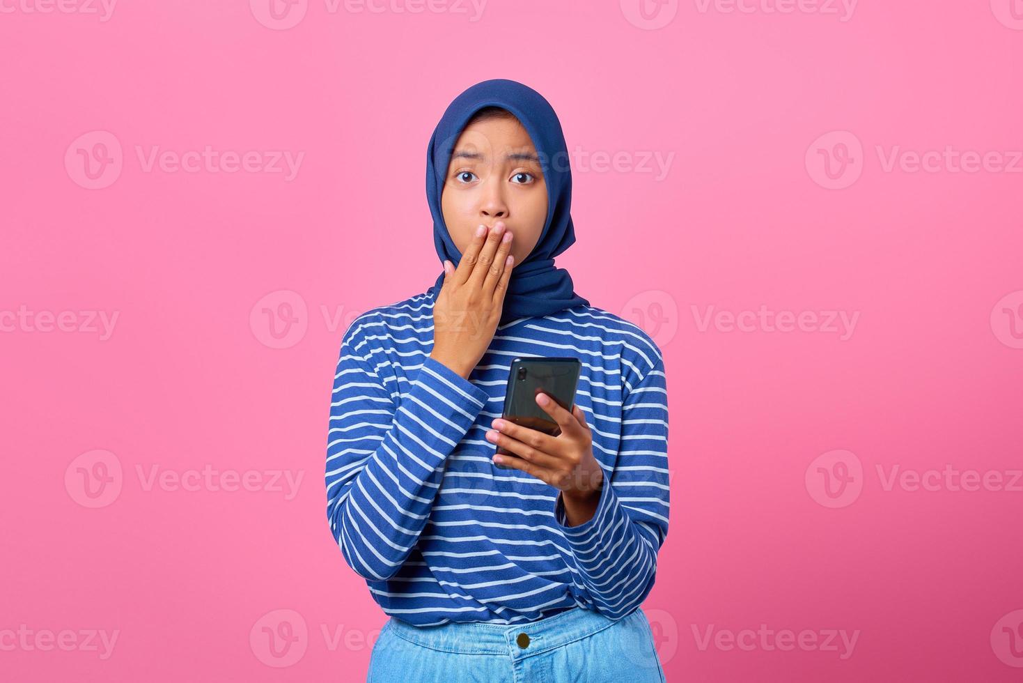 ritratto di una giovane donna asiatica scioccata che tiene in mano lo smartphone e si copre la bocca con la mano foto