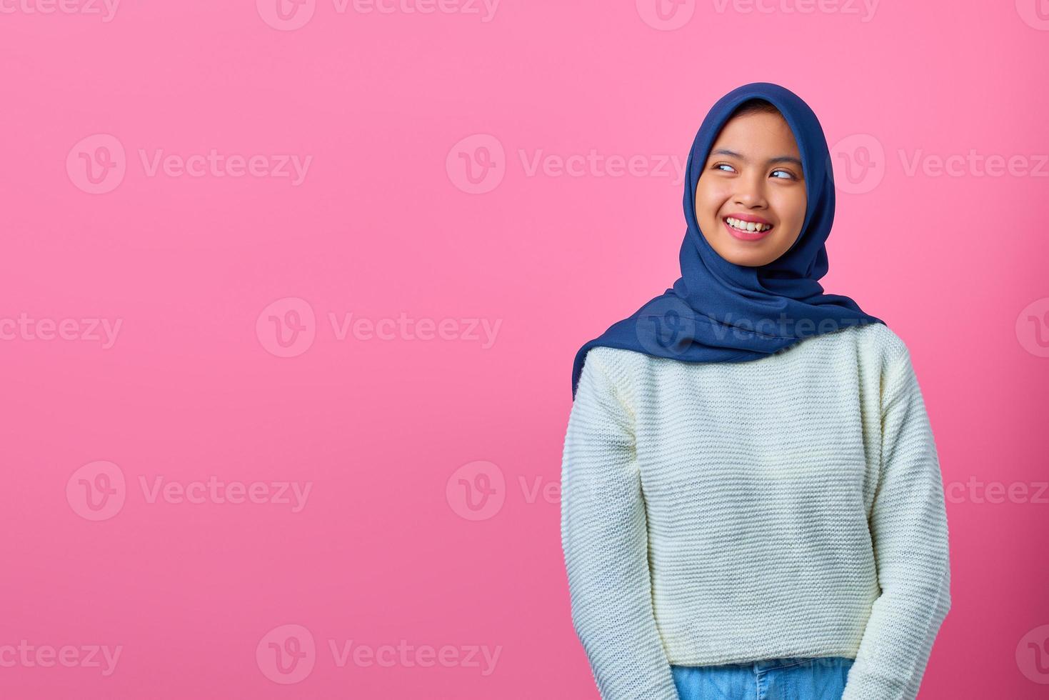 ritratto di giovane donna asiatica sorridente che guarda lontano a lato su sfondo rosa foto