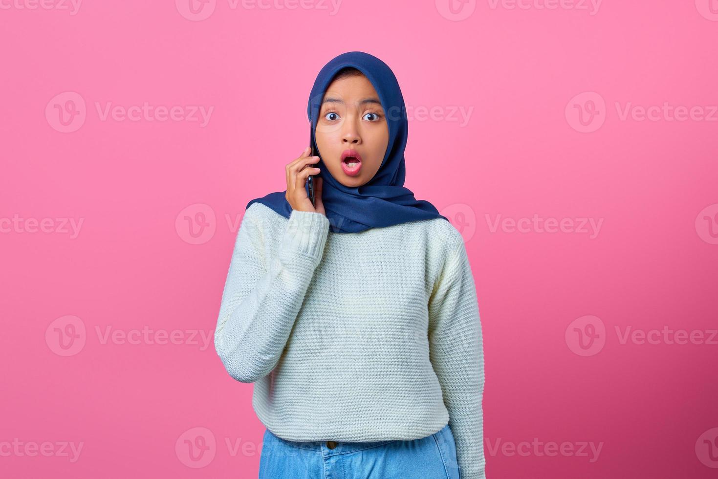 ritratto di giovane donna asiatica scioccata che parla su smartphone su sfondo rosa foto