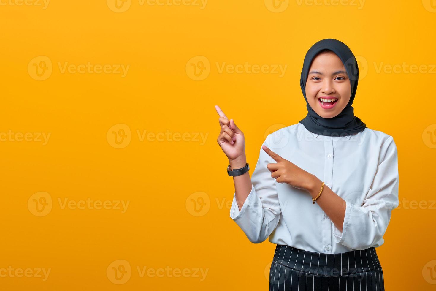 sorridente giovane donna asiatica che punta il dito sullo spazio della copia su sfondo giallo foto