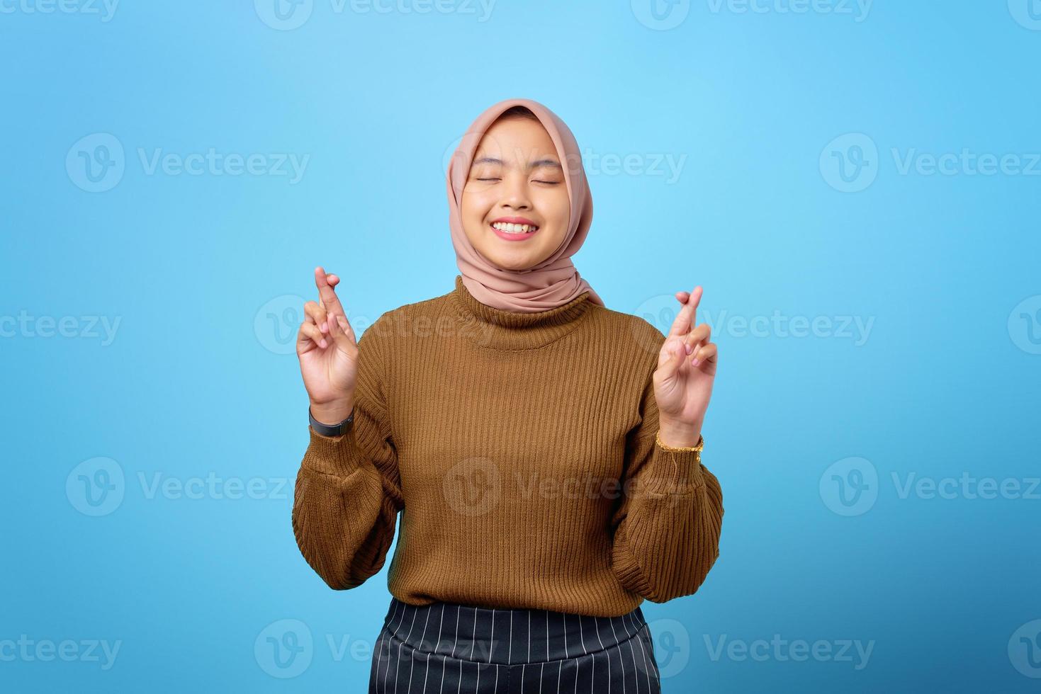 ritratto di felice giovane donna asiatica che incrocia il dito su sfondo blu foto