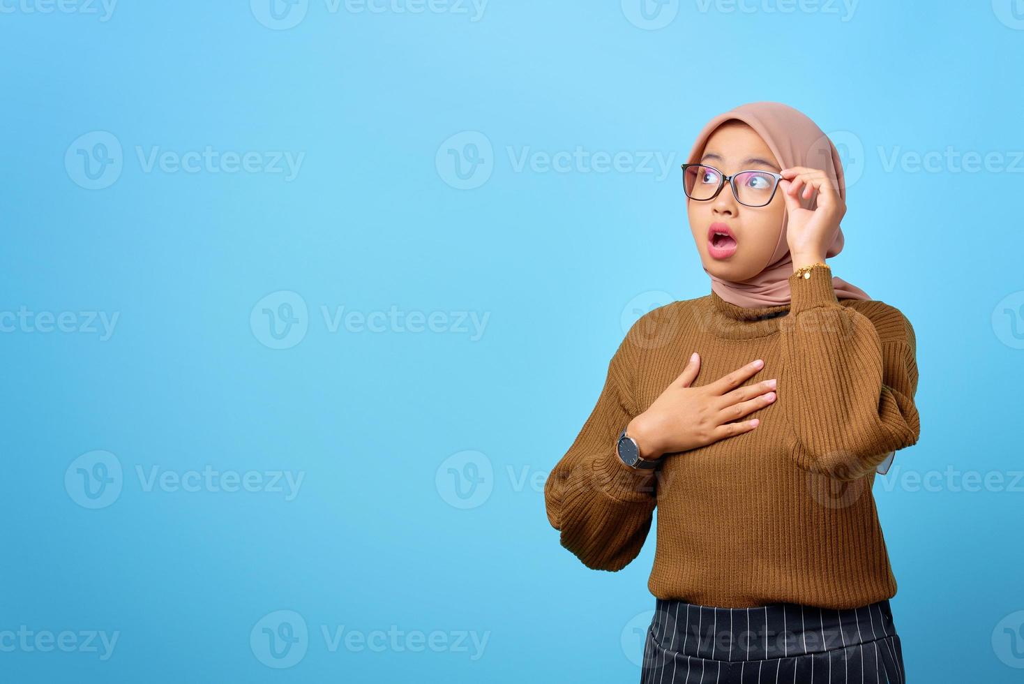 sorpresa giovane donna asiatica mano sugli occhiali con la bocca aperta su sfondo blu foto
