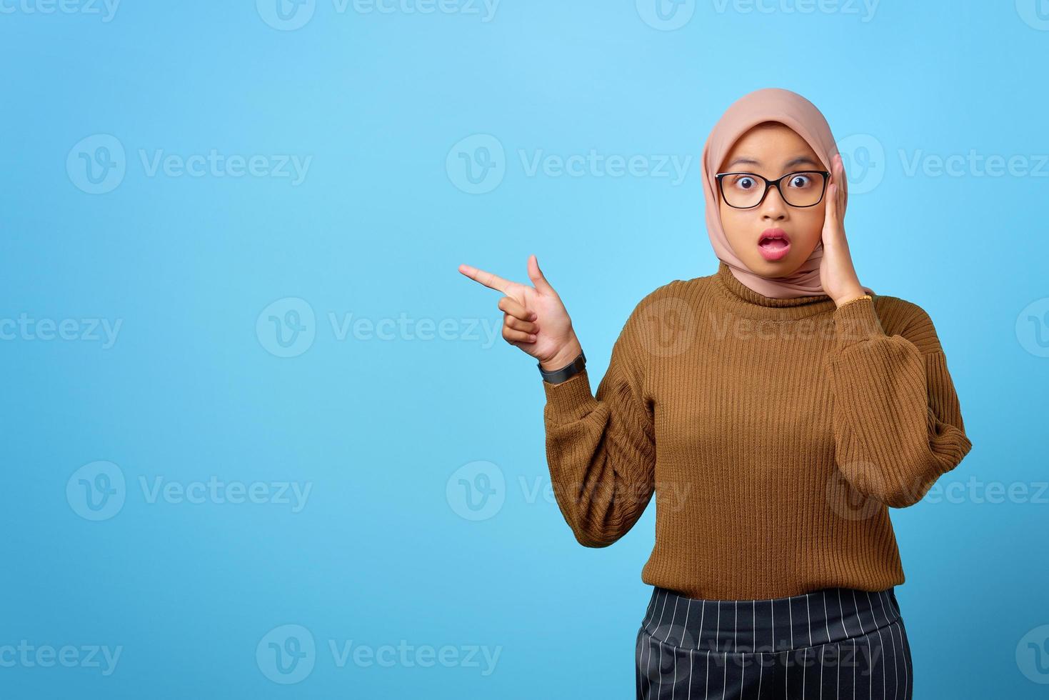 sorpresa giovane donna asiatica che punta il dito sullo spazio della copia su sfondo blu foto