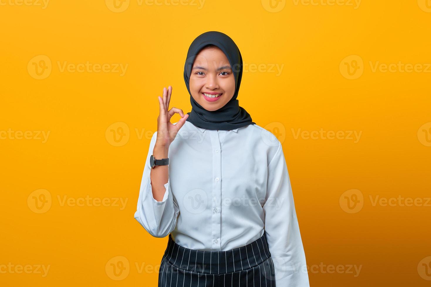 il ritratto di giovane donna asiatica felice fa il gesto giusto su fondo giallo foto