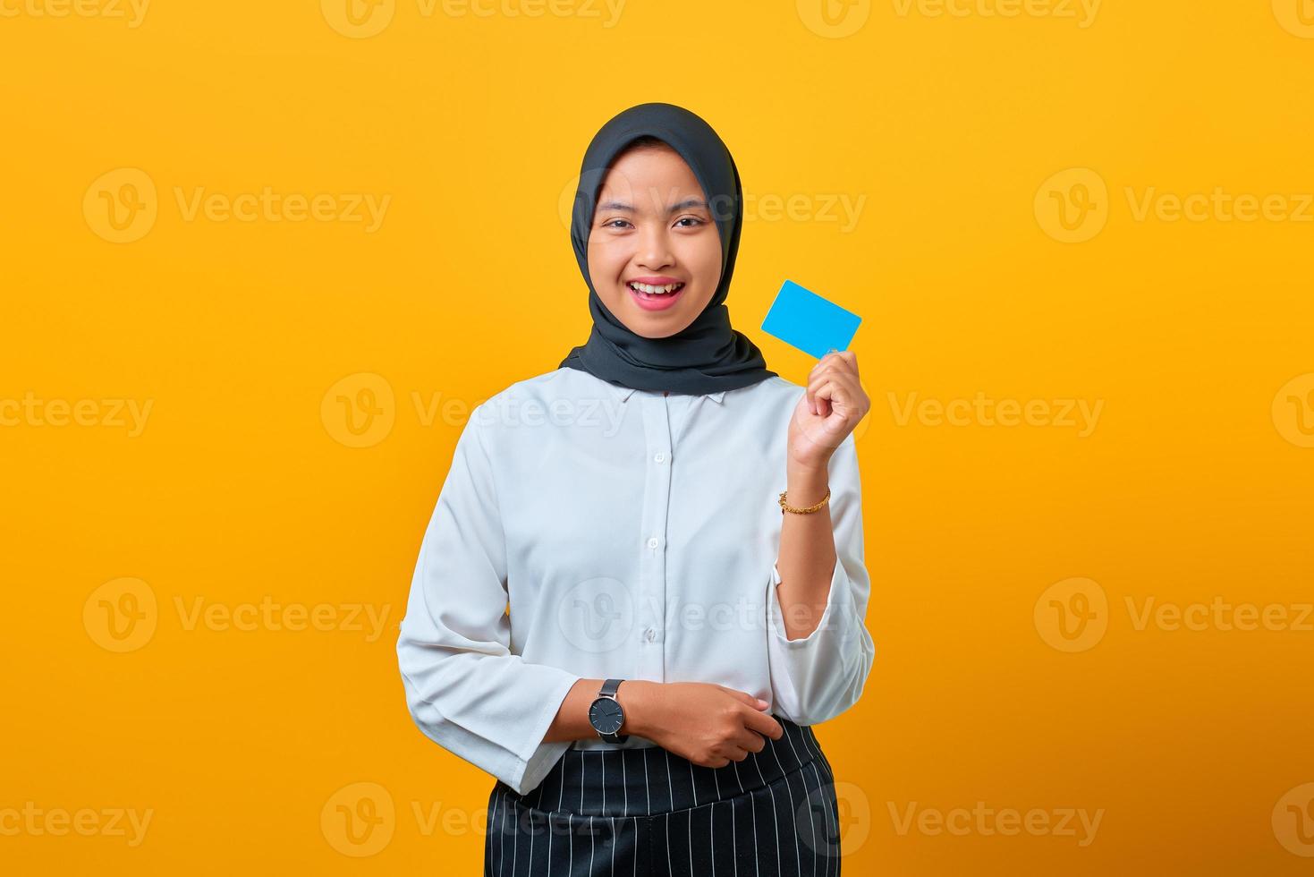 attraente giovane donna asiatica che ride e tiene in mano una carta di credito su sfondo giallo foto