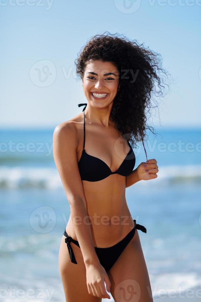 giovane donna araba con bel corpo in costume da bagno sorridente su una spiaggia tropicale. foto